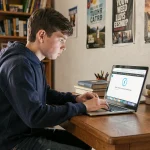 Élève adolescent frustré devant un écran d'ordinateur portable affichant une erreur de connexion internet, assis à son bureau dans sa chambre