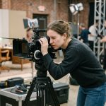 Étudiante en école de cinéma regardant dans le viseur d'une caméra professionnelle sur un plateau de tournage pédagogique